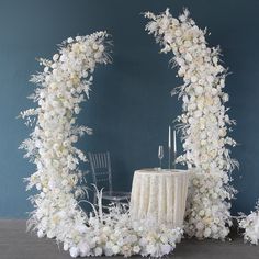 a white wedding arch decorated with flowers and candles on a table in front of a blue wall