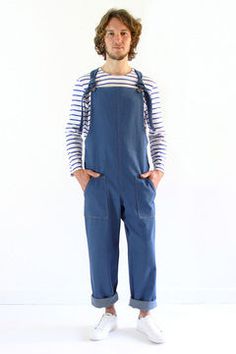 a man standing in front of a white wall wearing blue overalls and striped shirt