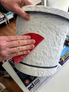 a person with their hand on the top of a white bucket that is sitting on a table