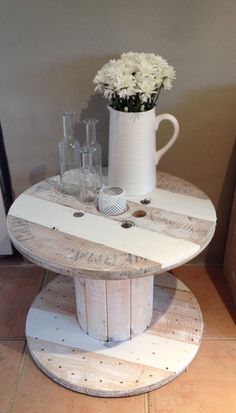 a white table with some vases on top of it and flowers in the middle