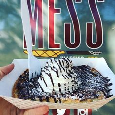 a person holding up a pastry in front of a sign with the word mess on it