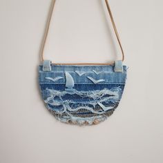 a purse made out of old jeans with birds flying over the ocean on it, hanging from a rope