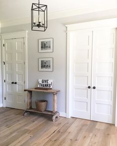 an empty room with white doors and pictures on the wall behind a wooden table that says give thanks