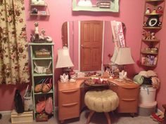 a bedroom with pink walls and lots of stuff on the desk in front of it