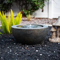 a water fountain sitting in the middle of a gravel area next to a potted plant