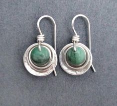 Raw genuine green emerald gemstones, weighing 1.8 carats each (3.6 carats/pair), are wrapped in sterling silver wire, then set within a sterling round dangle. Ear wires are also handcrafted in sterling silver wire. Artisan elegance and lightweight design make these earrings perfect for all day wear and comfort. Also are a great gift for a special someone with a May birthday, as emerald is May's birthstone. Raw genuine emeralds, 1.8 carats each (3.6 carats per pair), are opaque green with natural May Birthdays, Bronze Anniversary Gifts, Emerald Green Earrings, May Birthday, Peridot Earrings, Birthstone Earrings, May Birthstone, Anniversary Gifts For Wife, Sterling Silver Dangle Earrings