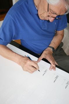 an older man sitting at a table writing on a piece of paper