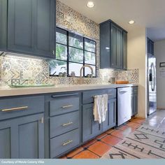 a kitchen with blue cabinets and tile flooring in the center, along with an area rug on the floor