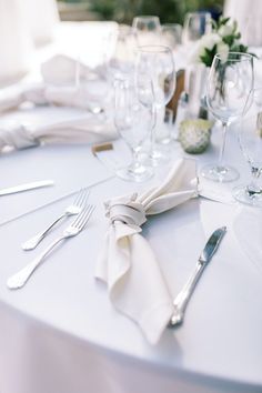 the table is set with wine glasses, silverware and white napkins on it