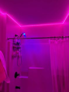 a bathroom with pink lighting and a shower head in the bathtub is lit up by purple lights