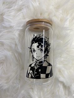 a glass jar with an anime character drawn on the front and sides, sitting on a fluffy white surface