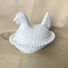 a white ceramic chicken sitting on top of a bowl