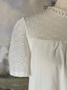 A charming historically inspired blouse that can be used in outfits ranging from the Edwardian era to the 1960's! This piece features a dainty eyelet lace yoke, scalloped lace mock-neck collar, short sleeves, and a gathered bodice. A versatile choice for building your historical wardrobe. This piece is part of our sustainable Secondhand, Vintage, and Upcycled Collection, and thus stock is limited to one! Sizing: Tag size XL, Fits like an XL.Bust up to 44 Inches / 110 CentimetersWaist up to 44 Inches / 110 CentimetersLength - 24.5 / 62 CentimetersSleeve Length - 8 / 22 CentimetersSleeve Width - 8 Inches / 22 Centimeters Condition: B | Some feeling of use, no major flaws. Materials: 100% Polyester synthetic "linen." Feminine Cotton Lace Patchwork Top, Spring Blouse With Peter Pan Collar And Lace Trim, Spring Blouse With Lace Trim And Peter Pan Collar, Cottagecore Short Sleeve Top With Lace Collar, Spring Cotton Lace Blouse With Broderie Anglaise, Spring Cotton Lace Blouse With Lace Work, Victorian Lace Trim Top For Daywear, Broderie Anglaise Cotton Lace Top, Victorian Cotton Tops For Spring