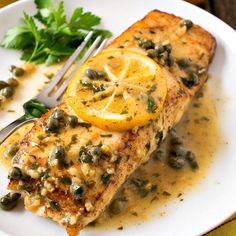 a piece of fish on a plate with lemons and capers