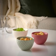 three bowls filled with food sitting on top of a white table next to two glasses