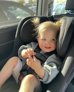 a young child sitting in a car seat with his hand on the steering wheel and looking at the camera