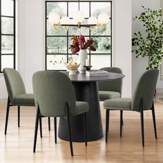 a dining room table with four chairs and a vase filled with flowers on it in front of a large window