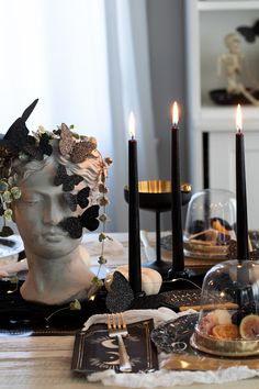 a table topped with candles and plates covered in black flowers next to a statue head