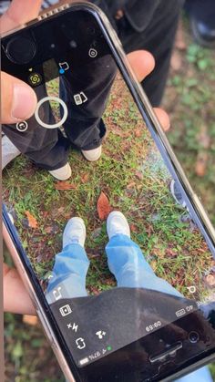 someone taking a selfie with their cell phone in the grass and feet on the ground