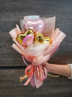 a person holding a bouquet of chocolates in their hand on a wooden table with pink ribbon