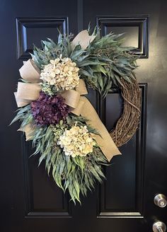 a wreath on the front door with flowers and greenery hanging from it's side