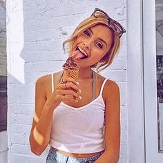 a woman eating an ice cream cone in front of a white brick wall and smiling