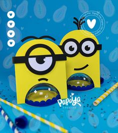 two small yellow boxes with eyes and noses on them, sitting next to candy sticks