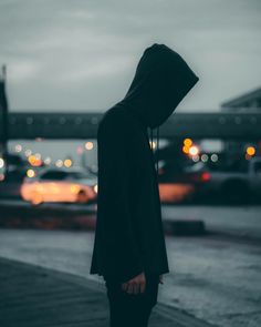 a person in a hoodie is standing on the sidewalk at night with their head turned to the side