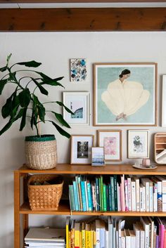 a bookshelf filled with lots of books next to a plant and pictures on the wall