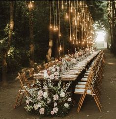 a long table set up with flowers and candles for an outdoor wedding reception in the woods