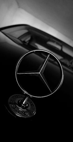 black and white photo of mercedes emblem on the hood of a car in front of a building