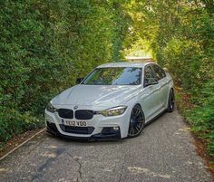 a white car parked on the side of a road next to some bushes and trees