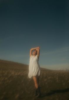 a woman in a white dress is standing in a field with her arms behind her head