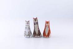 three small ceramic cats sitting next to each other on a white surface, with one cat looking at the camera