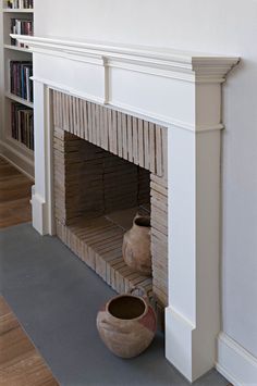 a white fireplace with two vases on the mantle and bookshelves behind it