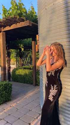 a woman in a black dress leaning against a metal wall with her hand on her face