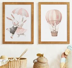 two framed pictures hang on the wall next to a basket and stuffed animals in hot air balloons