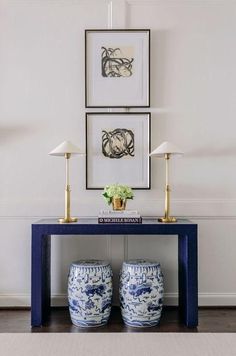 two blue and white vases sitting on top of a table in front of pictures