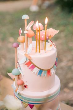 a pink cake with candles on top and decorations around the edges is sitting on a table outside