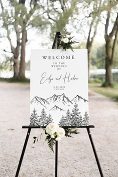 a welcome sign with flowers and greenery on it is displayed in front of some trees