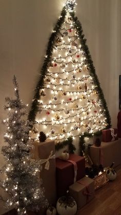 a christmas tree with presents under it and lights on the wall next to trees that are wrapped in brown paper