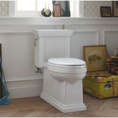 a white toilet sitting in the middle of a room next to a yellow suitcase and framed pictures