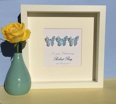 a blue vase with a yellow rose in it next to a framed butterfly art print