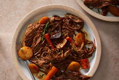 two plates with meat, carrots and other food items on them next to silverware