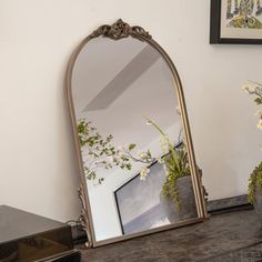 a mirror sitting on top of a table next to a vase with flowers in it