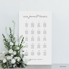 a wedding seating chart with white flowers and greenery on the table next to it