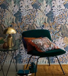 a green chair sitting in front of a blue wallpapered with flowers and leaves