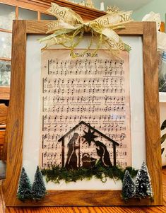 a frame with a nativity scene in the middle and christmas decorations around it on top of a wooden table