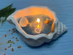 a candle that is inside of a shell on a table with flowers in the background