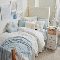 a white bed with blue and white comforter in a bedroom next to a window